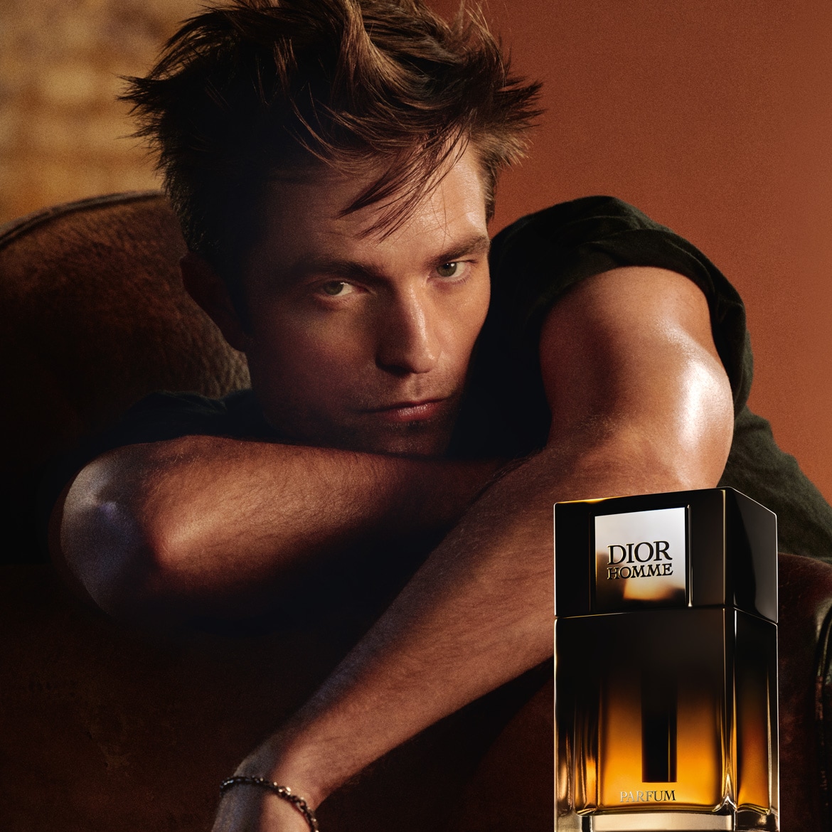 Robert Pattinson egy Dior Homme parfüm mellett pózol, a parfüm üvege fekete és arany színű, elegáns megjelenésű.