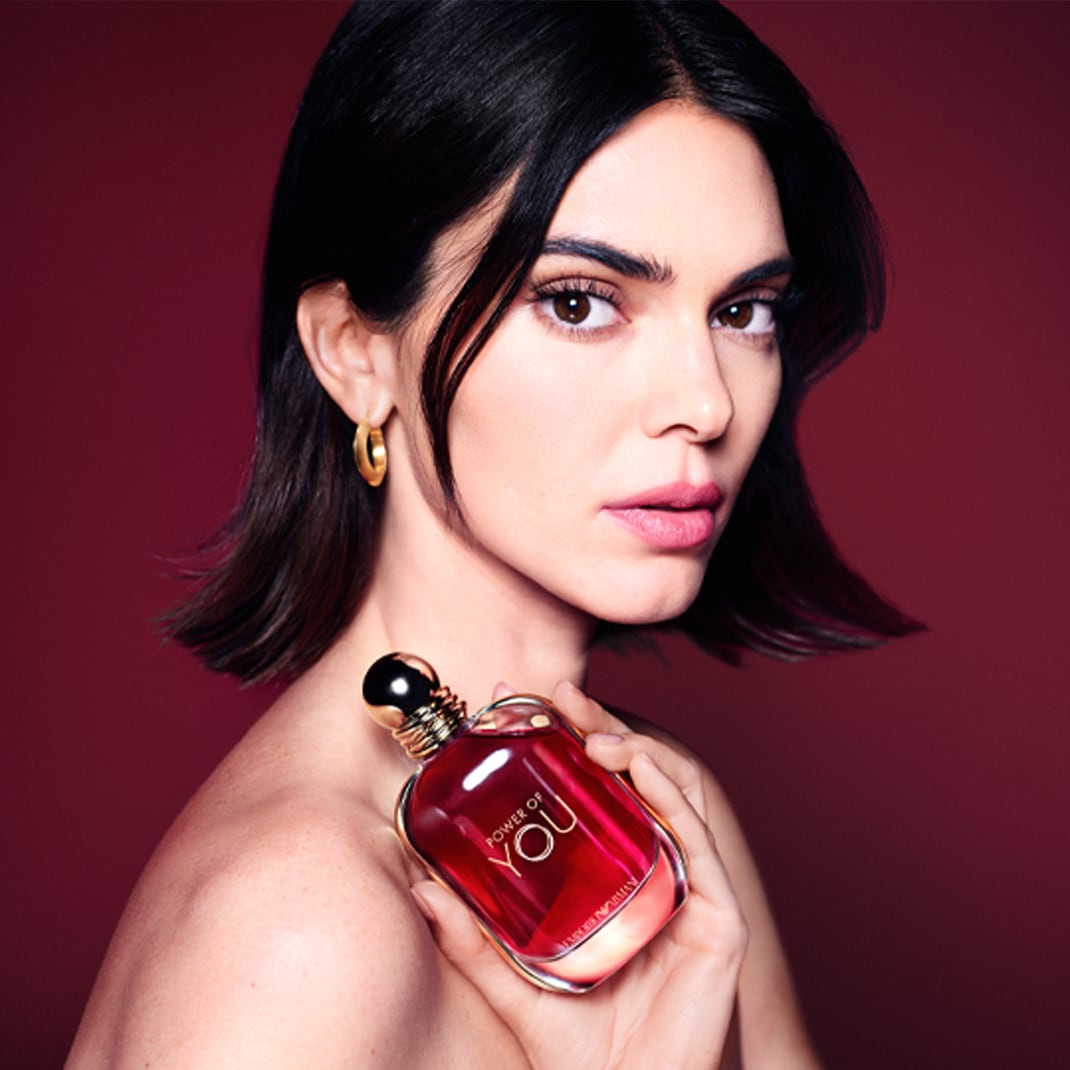 Egy nő portréja, aki egy piros, "Power of You" feliratú Armani parfümöt tart a kezében, a háttér is piros.