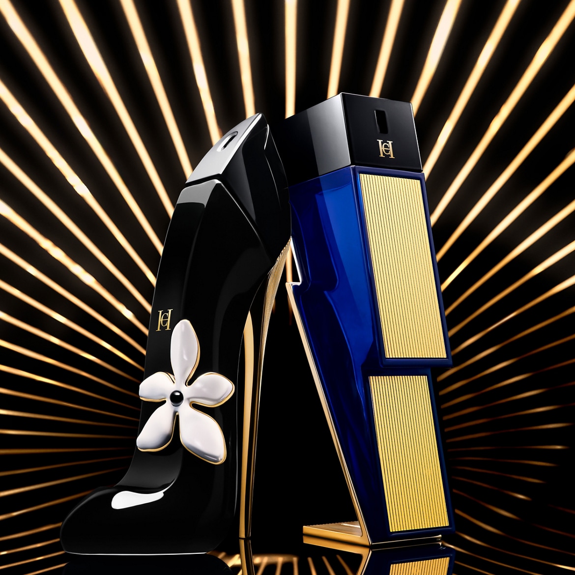 A Good Girl virágos illatú parfüm fekete magassarkúban, mellette egy Bad Boy kobaltkék és arany villám alakú parfümös üveg, mindkettő a Carolina Herrera márkától, arany csíkos háttér előtt.