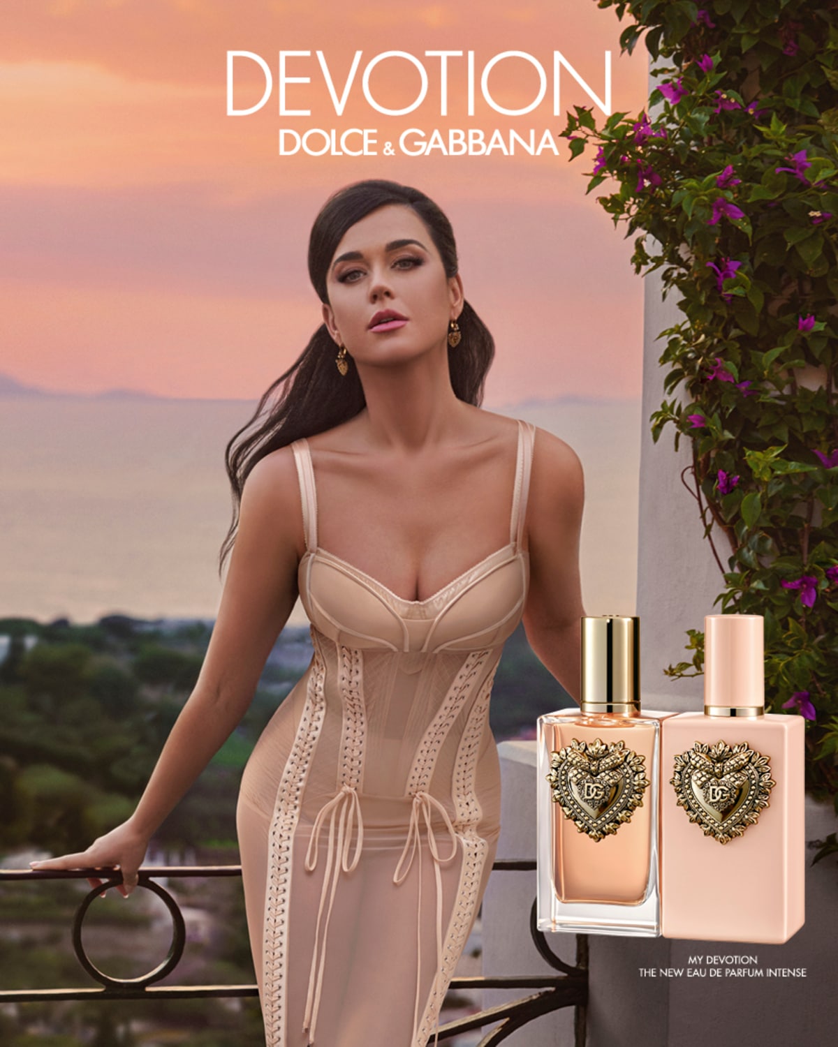 A Dolce & Gabbana Devotion parfümöt reklámozza a képen egy modell, a háttérben virágok és tenger látható, előtérben pedig a parfümös üvegek.