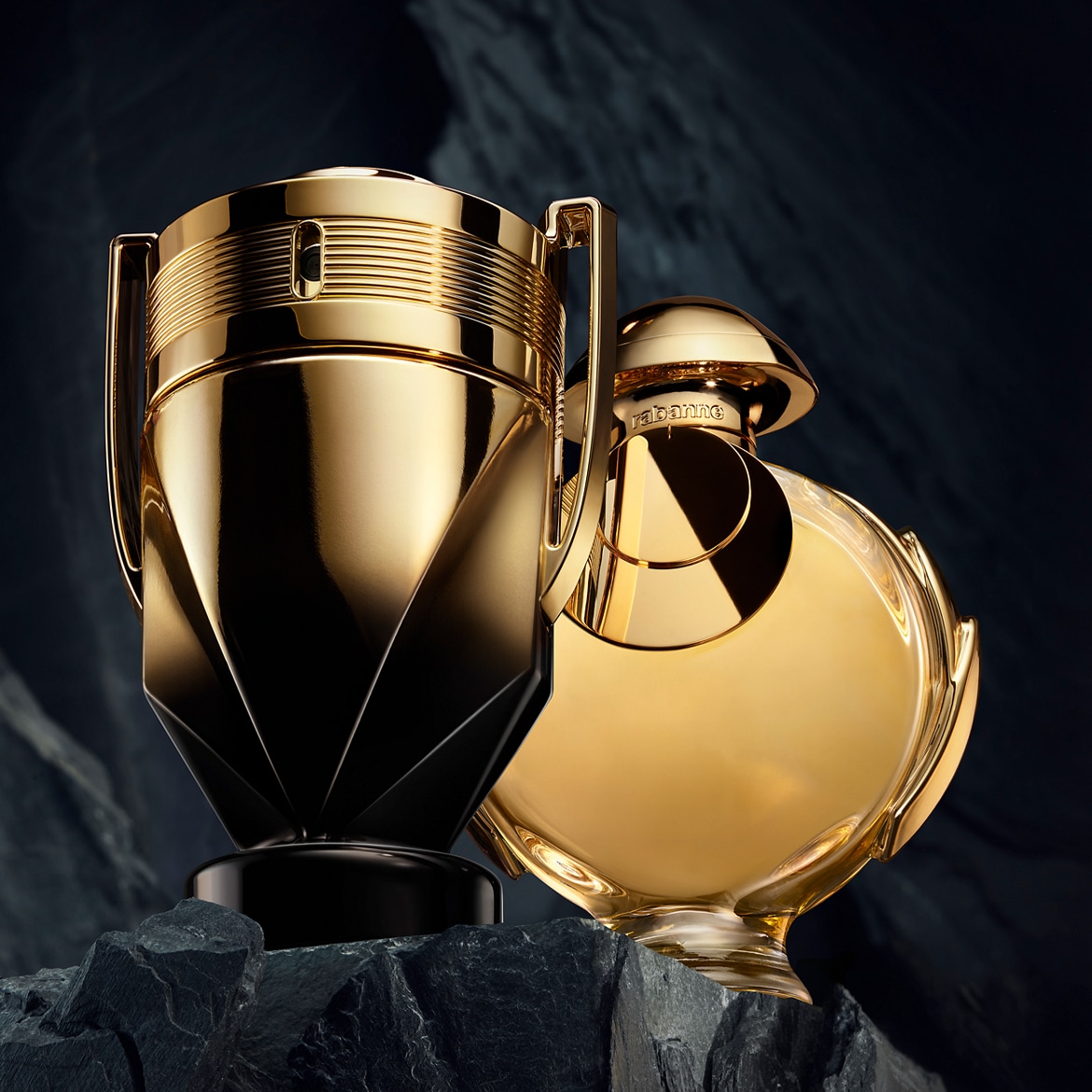 A Paco Rabanne Invictus és Olympea parfümök fényes arany trófeás üvegben, sziklákon ülve, a luxust és a győzelmet sugározzák.