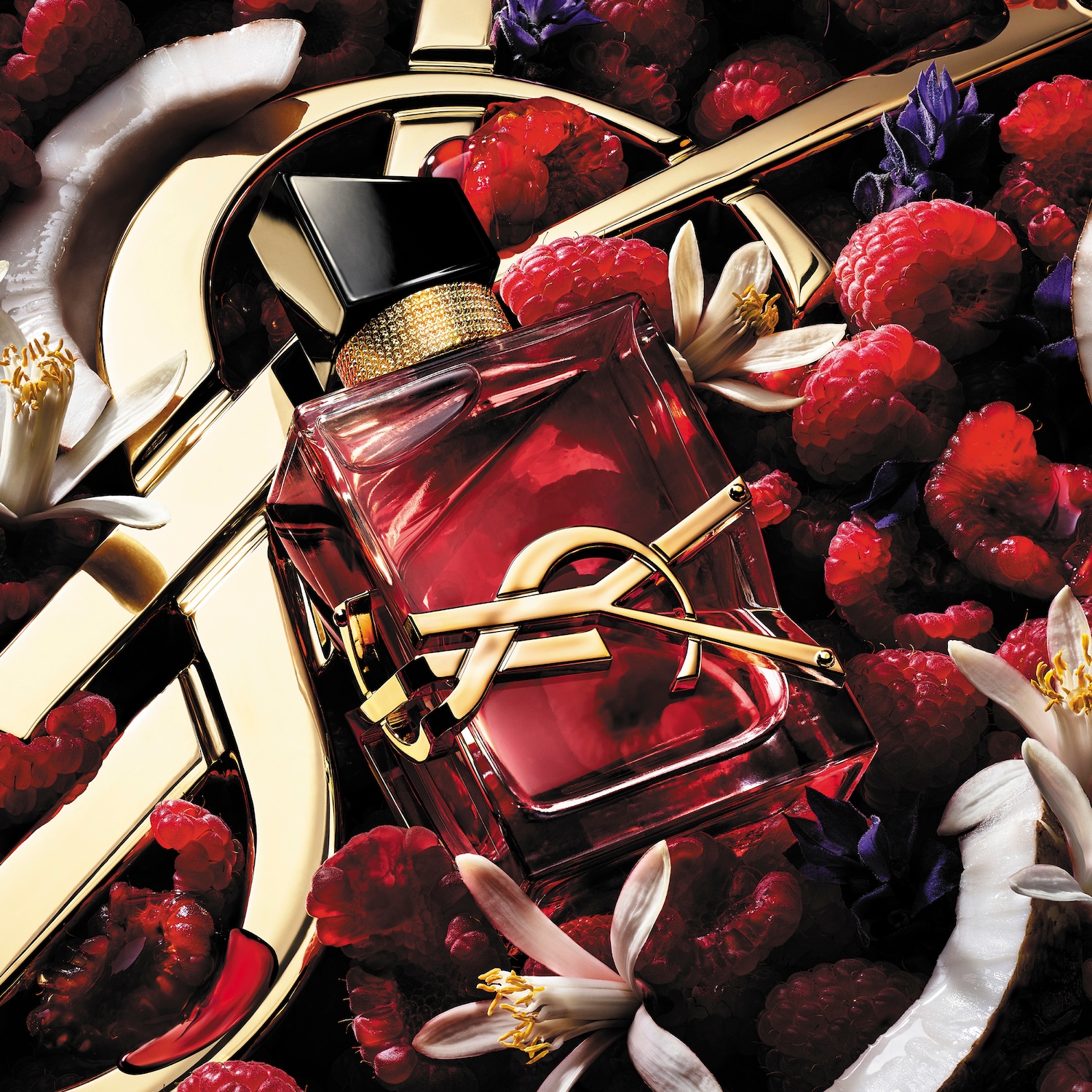 A fényes, piros színű YSL illatüveg arany logóval, friss málna, kókusz és virágok között helyezkedik el.
